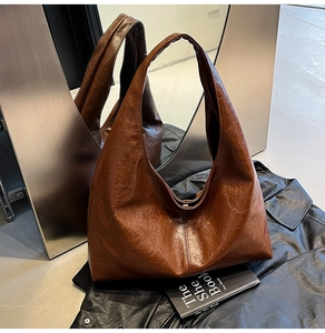 Detailed view of brown pleated faux leather tote bag with glossy finish and wide strap