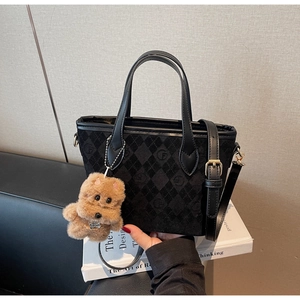 Detail of black quilted handbag with embossed logos and a brown plush dog charm