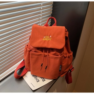 Detail of orange canvas backpack showing drawstring closure and embroidered flap logo