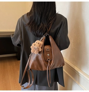 Detail of brown leather tote featuring silver flower buckle, fringe, and plush bear charm