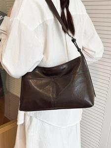 Dark brown leather tote bag with adjustable strap worn by a model in casual style