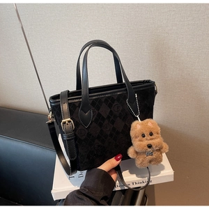 Detail view of black textured bucket bag with leather handles and a plush bear charm