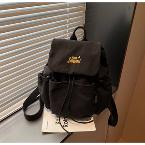 Detail of black canvas backpack featuring yellow embroidery and drawstring closure