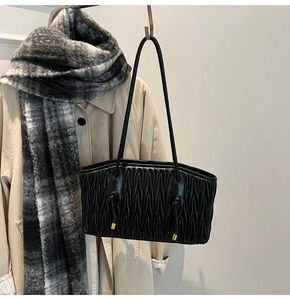 Detail of black pleated tote bag with knot decor and gold metal tips on trench coat