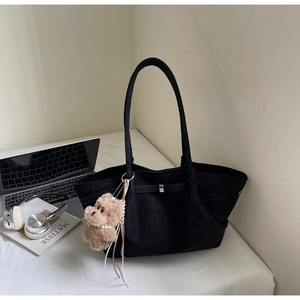 Detail of black suede tote bag with metal buckle and plush dog charm in office setting