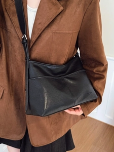 Fashionable black faux leather tote bag with adjustable strap worn by a model in casual style