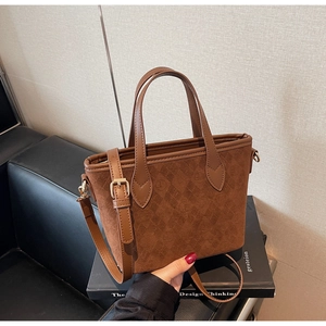 Detailed macro view of the brown suede tote bag featuring embossed logo texture and gold buckles