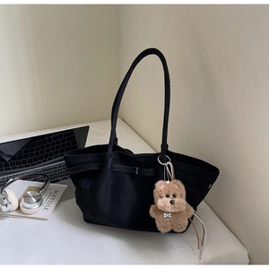 Detail of black suede tote bag with plush dog charm and minimalist office accessories