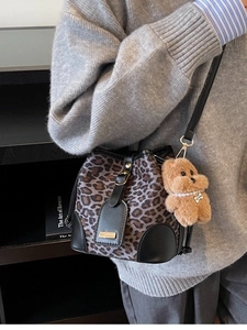 Leopard print bucket bag with leather trim and bear charm shown in a crossbody style