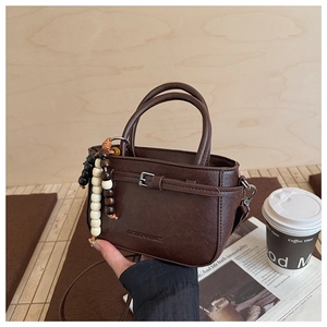 Detail of a brown vintage leather crossbody bag with beaded charm and buckle detail