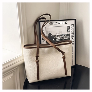 Detail of minimalist cream tote bag with brown leather handles on a glossy black surface
