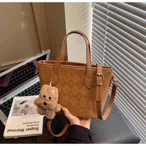 Detail of brown tote bag with embossed circular patterns and cute plush puppy charm