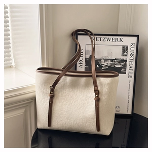 Close-up of off-white lychee texture tote bag with brown leather handles and brass buckles
