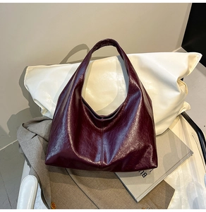 Detail view of burgundy tote bag with pleated leather texture on a white pillow