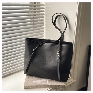 Close-up of black lychee grain leather tote bag with adjustable strap and golden buckle