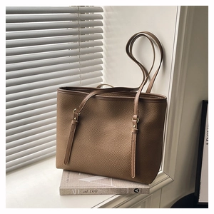 Detail of a brown leather tote bag with lychee grain texture and gold metal rivets