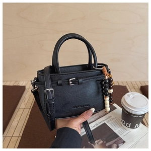 Detail of a black mini Boston bag with lychee texture and wooden bead charm detail