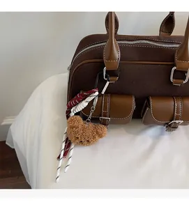 Détail d'un sac Boston en daim marron avec poches à rabat et breloque ours en peluche