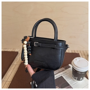 Detail of black mini faux leather handbag with beads charm and embossed fashion text