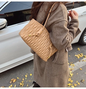 Detail of beige matelassé pleated tote bag with drawstring on brown wool coat