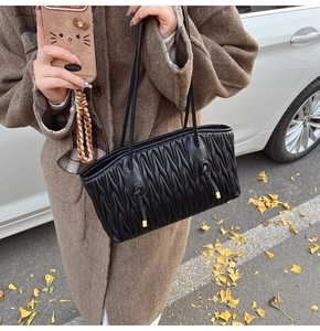 Detail of black pleated tote bag with golden metal accents and double slim straps