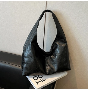 Detail of minimalist black patent leather hobo bag with glossy wrinkled texture on sofa