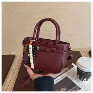 Close-up of wine red leather handbag with strap and colorful ethnic beaded charm detail