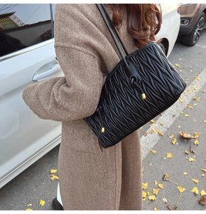 Detail of black matelassé quilted tote bag with thin leather straps on a brown wool coat