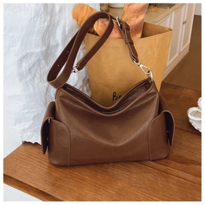 Détail macro du sac bandoulière en cuir marron avec poches latérales et boucles argent