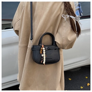 Detail of black leather square crossbody bag with decorative wooden beads and embossing