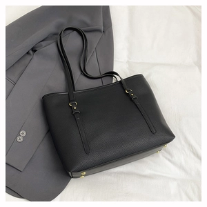 Detail of black pebbled leather tote bag with gold buckle accents and protective feet