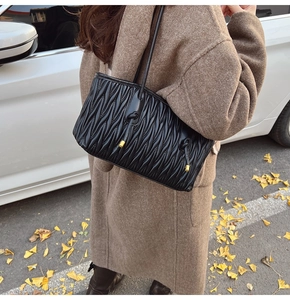 Close-up of black pleated hobo bag with gold-tipped drawstring detail on model