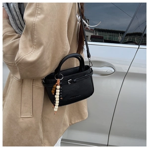 Detail of a chic black trapezoid crossbody bag with colorful beaded charm in street style