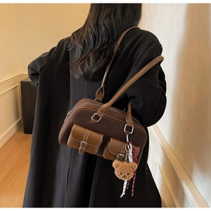 Détail d'un sac Boston marron avec poches avant, breloque ourson et décor en foulard