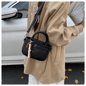 Detail of a black leather crossbody bag with wooden bead pendant in an outdoor setting