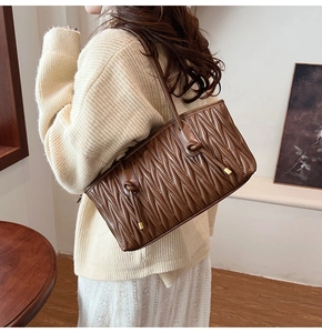 Brown matelassé quilted leather shoulder bag shown on model in a cozy indoor setting