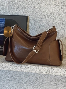 Sac bandoulière minimaliste en cuir marron foncé poli sur une surface en pierre grise