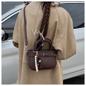 Detail of a dark brown mini handbag with beaded pendant and adjustable strap in use