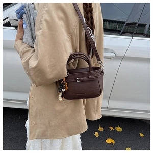 Detail of dark caramel crossbody bag with wooden beads and strap on autumn street