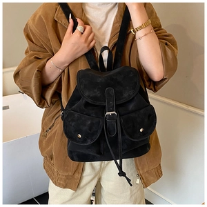 Close-up of black suede backpack featuring dual front pockets and gold buckle details