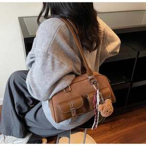 Détail d'un sac à bandoulière marron avec coutures blanches et breloque ours en peluche