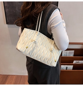 Detail of white matelassé pleated tote bag with gold drawstring and shoulder strap