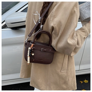 Detail view of brown leather crossbody bag with decorative wood beads and metal buckle