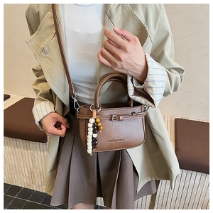 Detailed shot of brown mini crossbody bag featuring pearl beads charm and leather texture