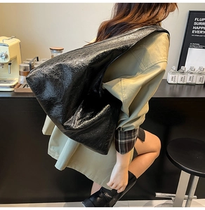Model wearing a large minimalist black crinkled patent leather hobo tote shoulder bag