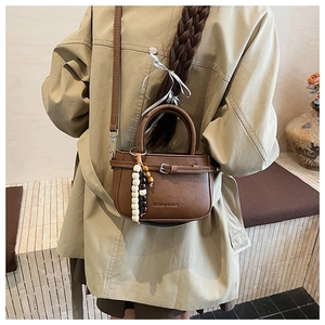 Detail of a brown leather crossbody bag with beaded charms and fashion logo on casual strap