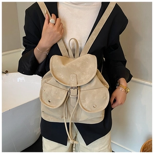 Close-up of beige suede backpack showing buckle flap and dual metal snap pockets