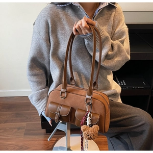 Détail du sac Boston en daim marron avec garniture en cuir et breloque ours en peluche