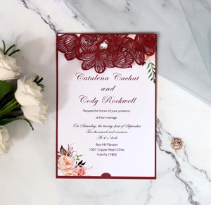 Detail view of burgundy laser-cut wedding invitation on elegant white marble background