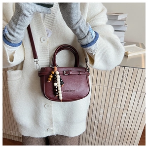 Detail of burgundy mini square bag with beaded charm on a soft white knit sweater